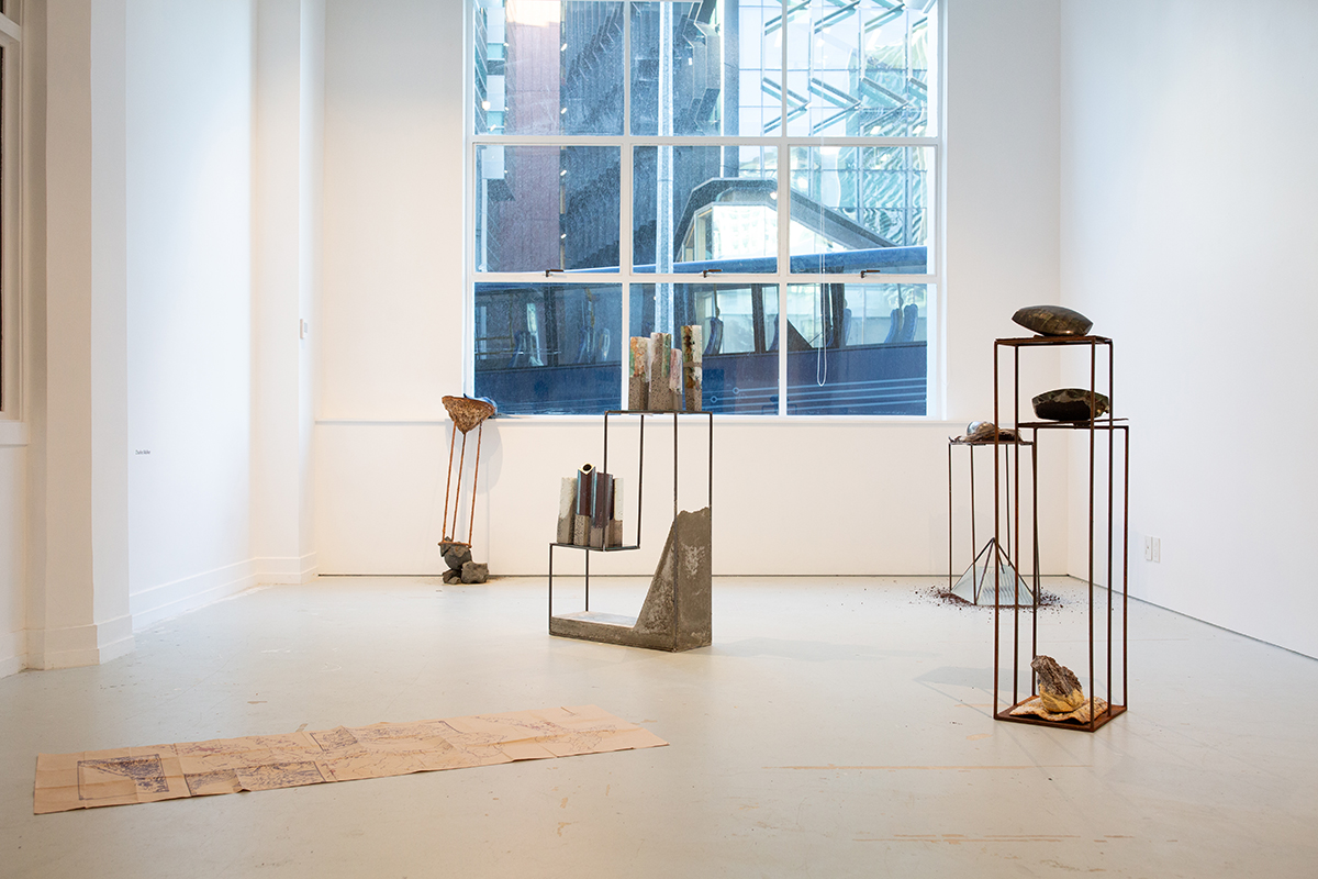 Installation view, map on floor, metal plinths displaying objects