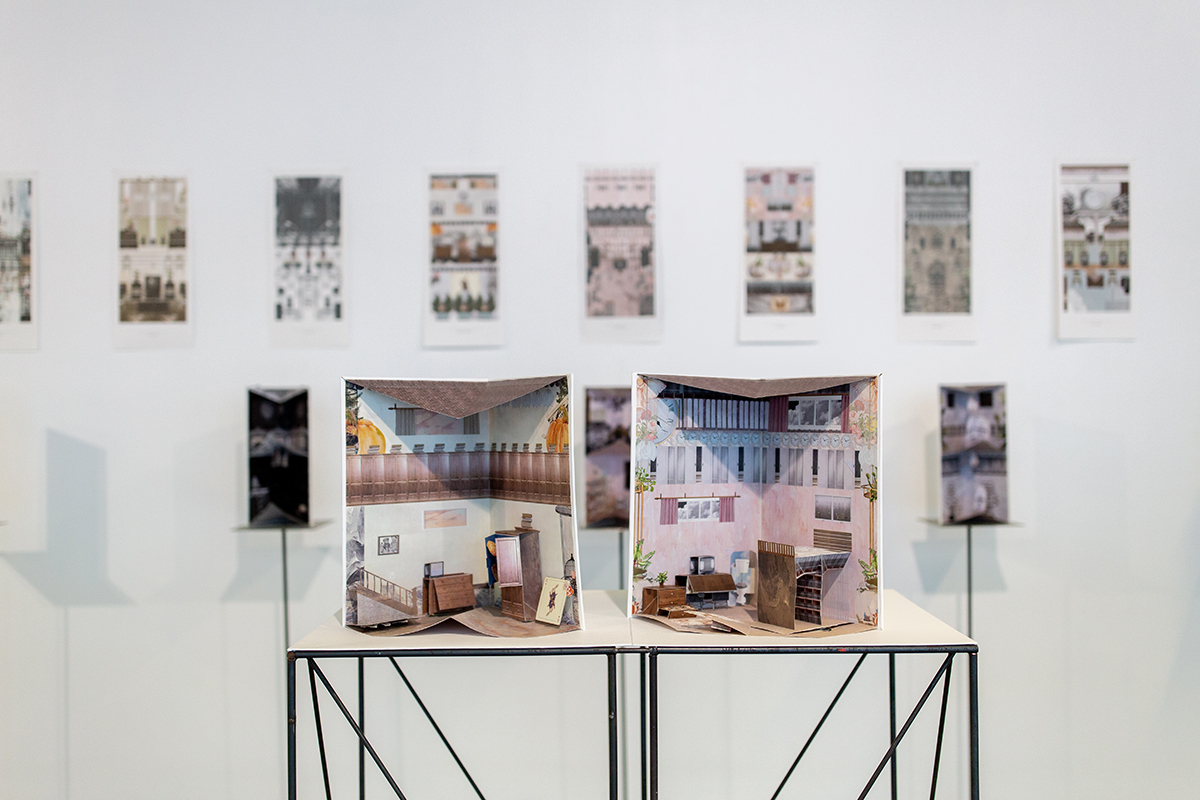 Posters along back wall and paper-constructed rooms on plinths